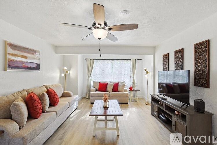 A living room with a beige sofa, a wooden coffee table, a flat screen TV, and a ceiling fan.