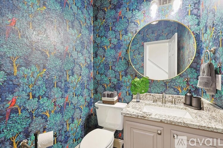 A bathroom with a white toilet, a sink with a mirror above it, and a wallpaper with a bird pattern.