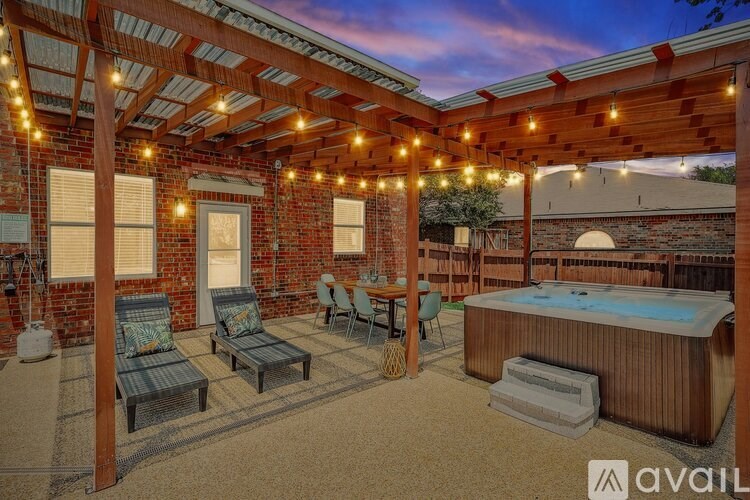 A patio with a hot tub and chairs under a pergola.
