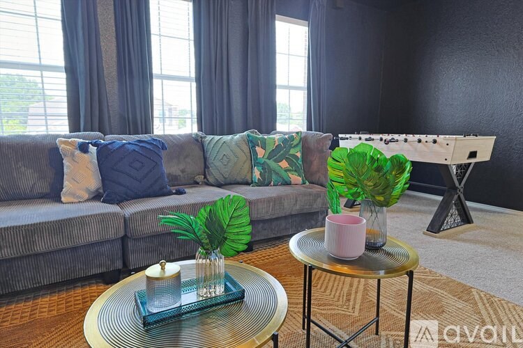 A living room with a grey couch, a coffee table with a pink candle, and a plant on it.