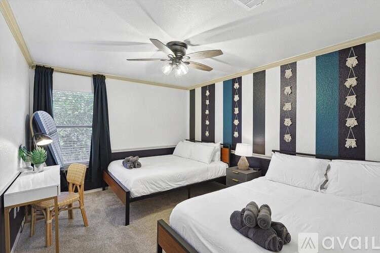 A bedroom with two beds, a desk, and a ceiling fan.