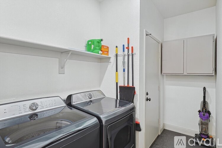 A small laundry room with a washer and dryer, a broom, a mop, and a green bucket.