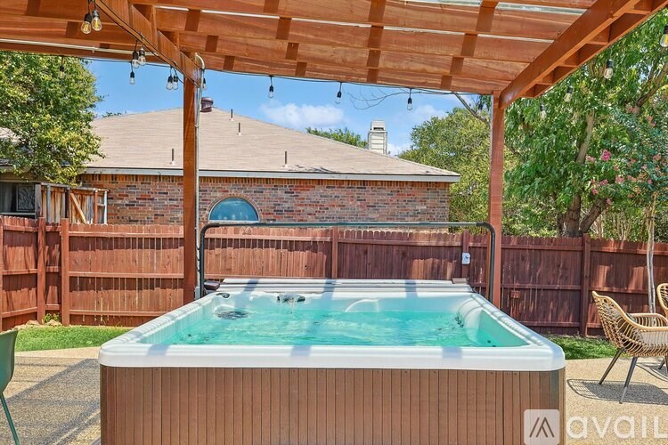 A hot tub is under a wooden pergola in a backyard.