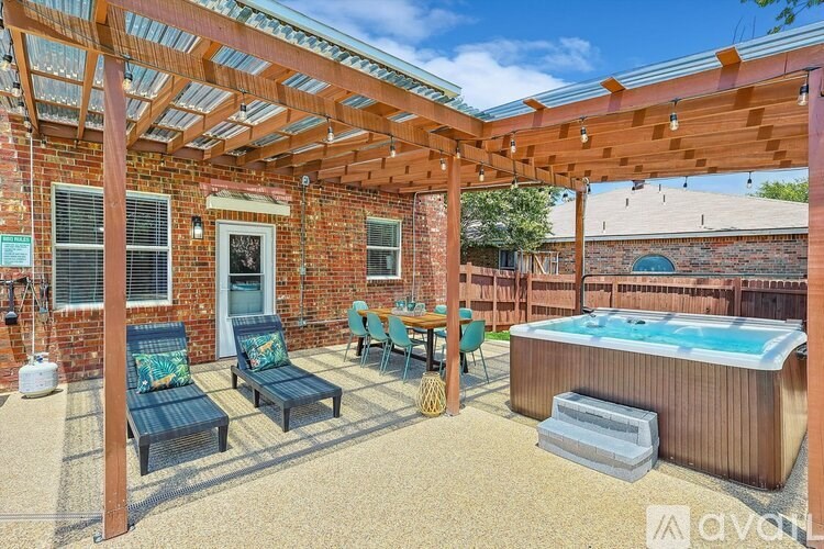 A patio with a hot tub and chairs under a pergola.