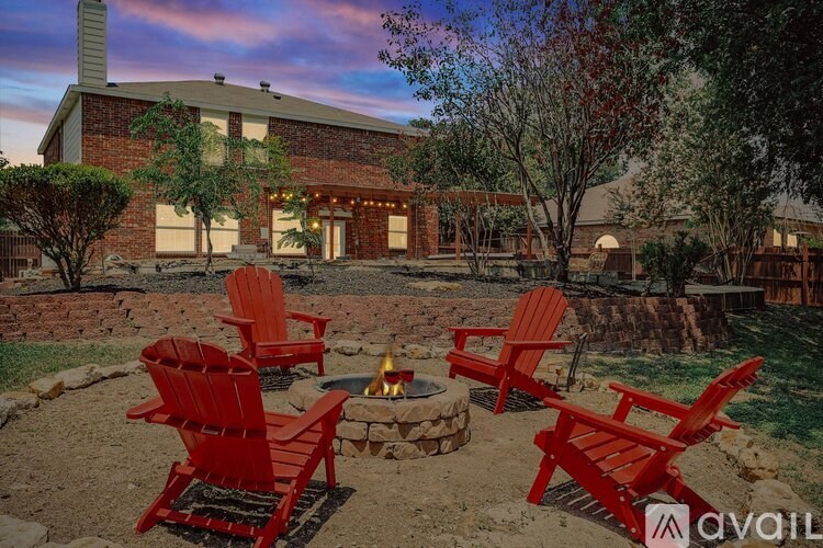 A house with a fire pit and four red chairs in front.