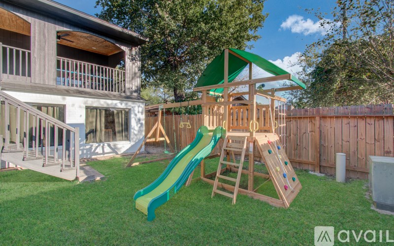 A wooden swing set with a green slide in a backyard.