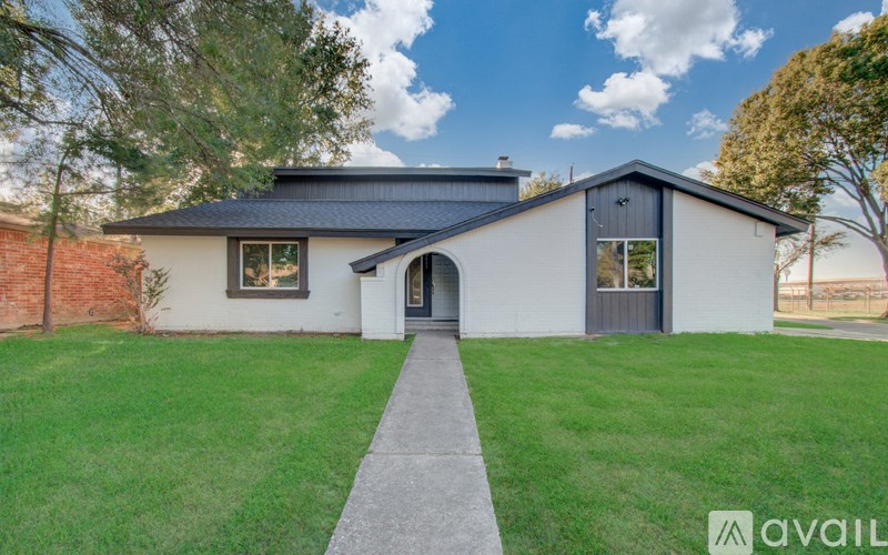 A house with a grey roof and a white exterior is surrounded by a green lawn.