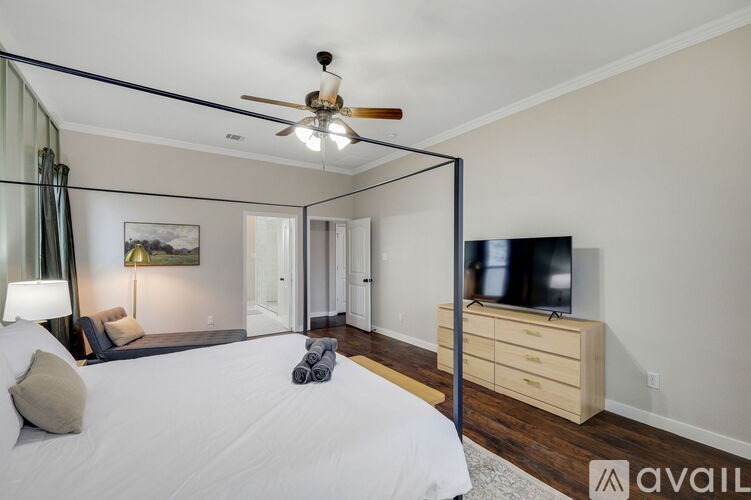 A bedroom with a bed, a ceiling fan, a television, and a lamp.