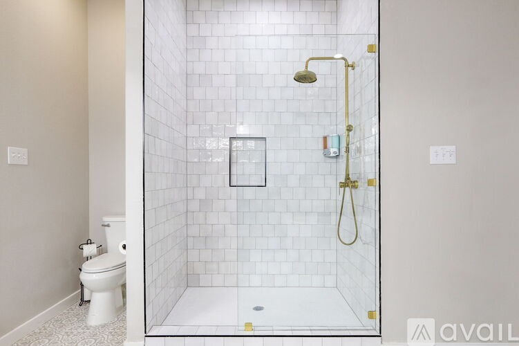 A white tiled shower with a gold shower head and faucet.