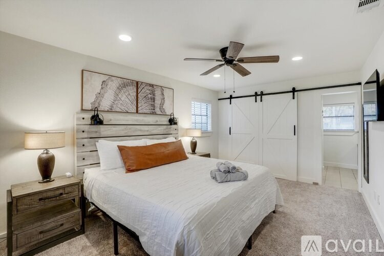 A bedroom with a large bed, a ceiling fan, and a painting on the wall.