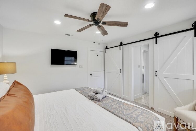 A bedroom with a bed, a ceiling fan, and a television mounted on the wall.