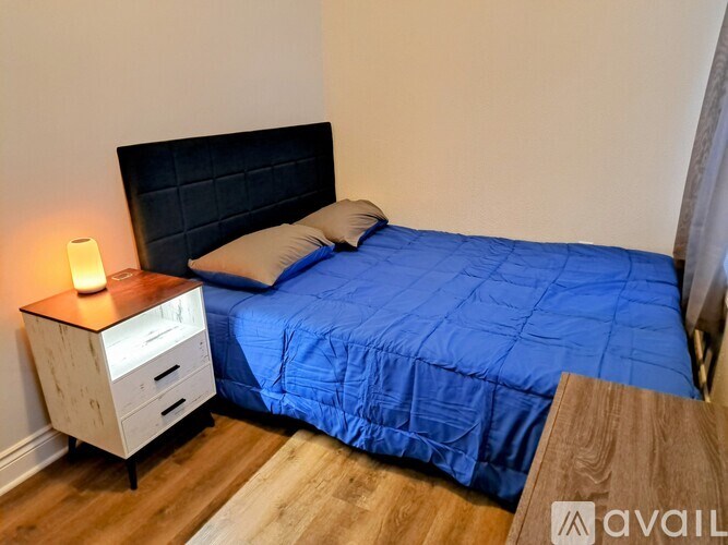 A bed with a blue comforter and a wooden nightstand with a lit candle on it.