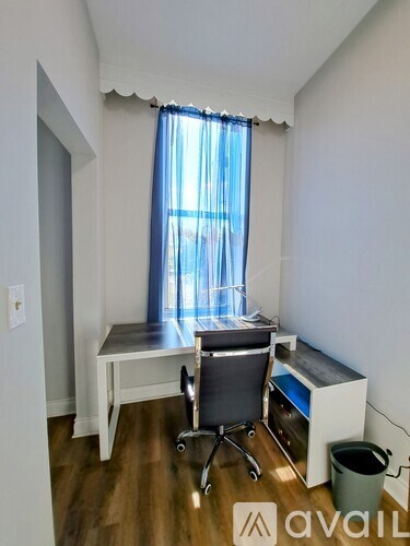 A room with a desk, chair, and window with curtains.