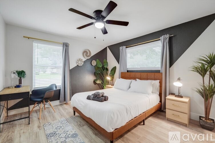 A bedroom with a bed, desk, chair, and ceiling fan.