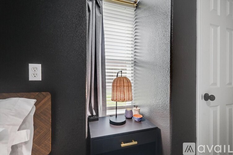 A lamp with a brown shade sits on a black dresser next to a window with blinds.
