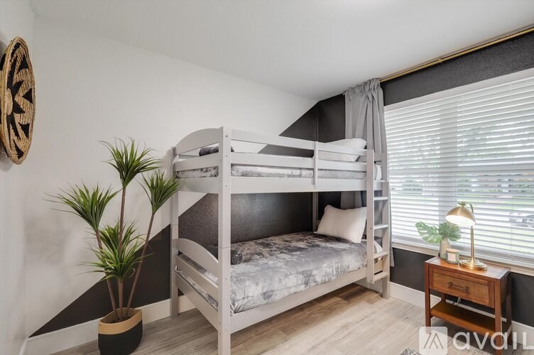 A white bunk bed with a grey blanket and pillow is in a room with a plant and a wooden table.