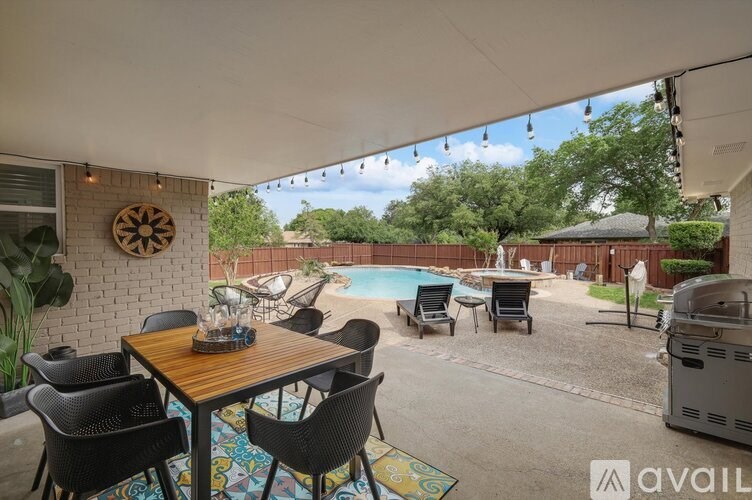 A patio with a table and chairs is set up with a pool in the background.