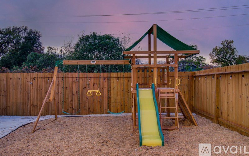 A wooden swing set with a green canopy and a yellow slide in a backyard.