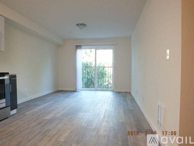 A spacious living room with wooden flooring and a sliding glass door leading to a balcony.
