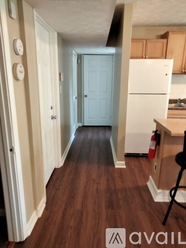 A hallway with a white door and a white refrigerator in the kitchen.