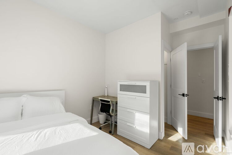 A white bedroom with a bed, nightstand, and a small table with a chair.