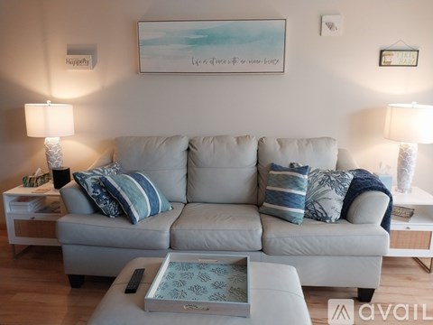 A living room with a grey couch and a painting on the wall.