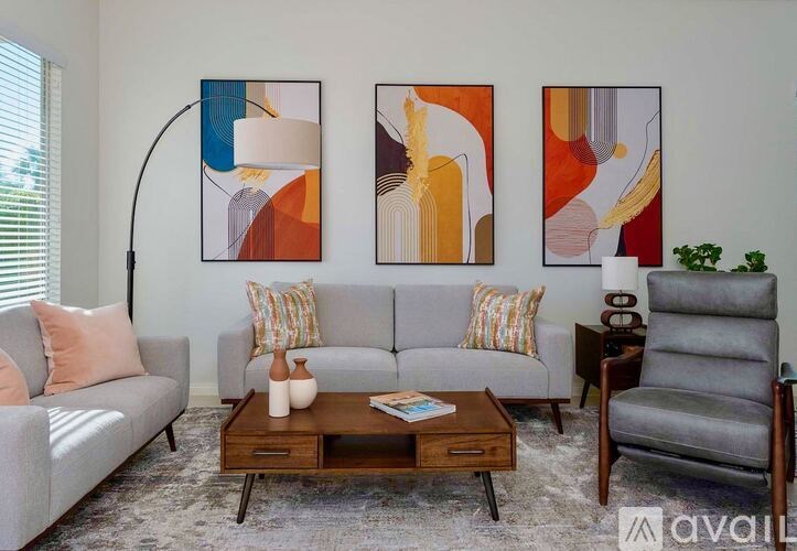 A living room with a grey couch, a coffee table, a lamp, and three abstract paintings on the wall.
