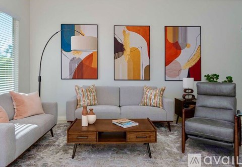 A living room with a grey couch, a coffee table, a lamp, and three abstract paintings on the wall.