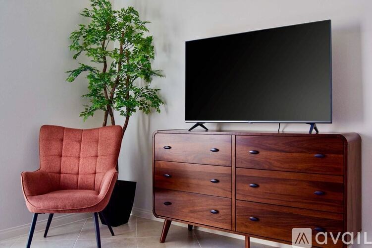 A red chair sits next to a wooden chest of drawers and a black television.