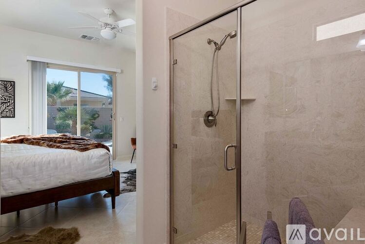 A bedroom with a bed, a ceiling fan, and a walk-in shower.