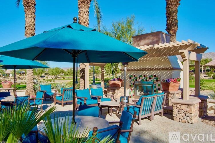 A blue umbrella shades a table with chairs under a pergola.