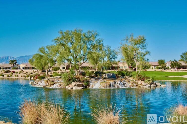 A serene lake surrounded by houses and trees under a clear blue sky.