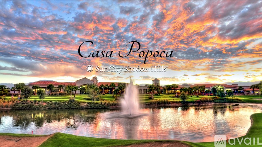 A beautiful sunset view of a golf course with a fountain in the foreground and a building in the background.