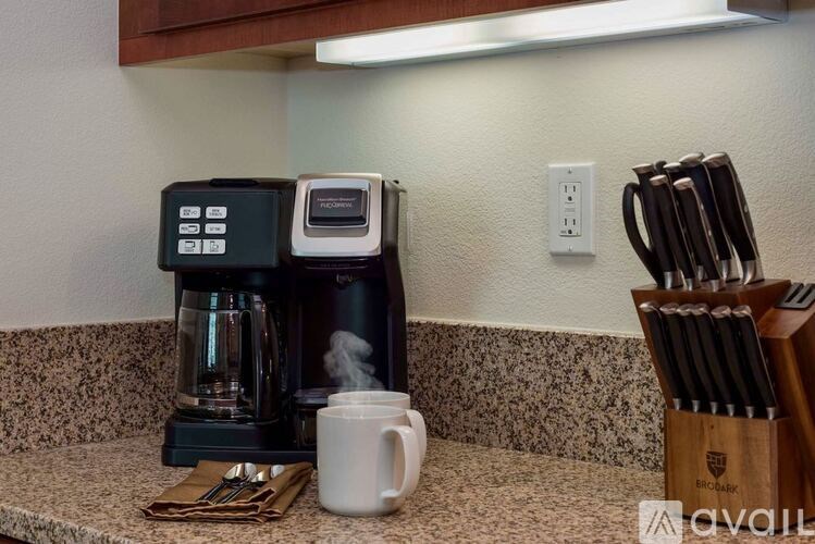 A coffee maker is on a counter with a cup and a set of knives.