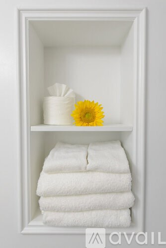 A white towel is folded and stacked on top of another white towel in a white shelf.