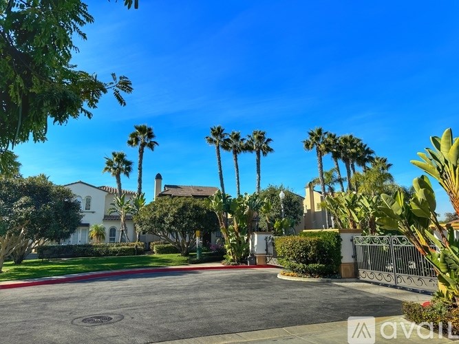 A gated community with palm trees and a white house in the background.