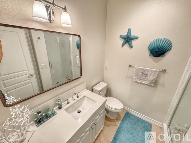 A bathroom with a white sink, toilet, and a blue rug.
