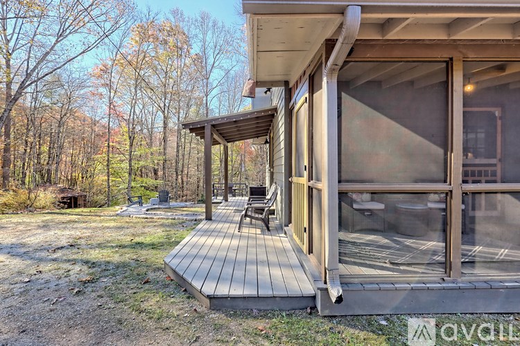 A wooden deck with a bench and a pergola is surrounded by trees.