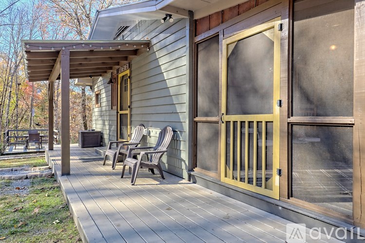 A wooden deck with chairs and a table is on the left side of a house with a glass door.