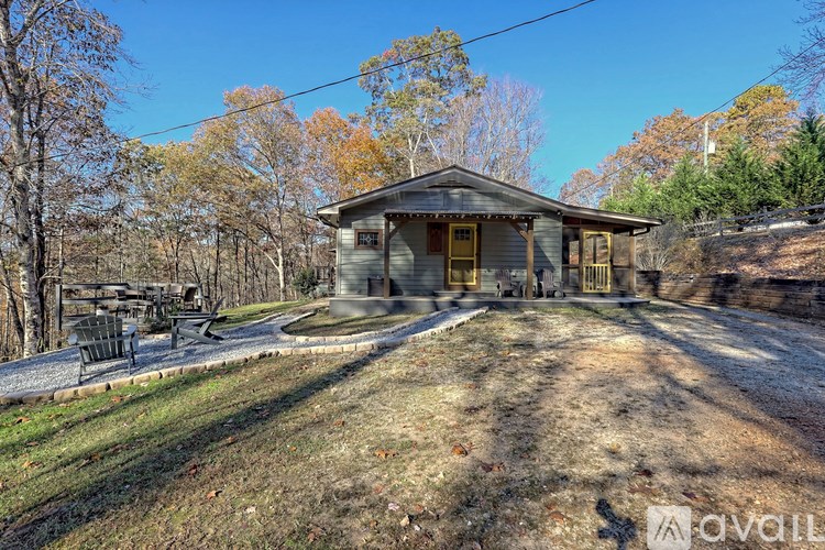 A house with a porch and a yellow door is surrounded by trees.