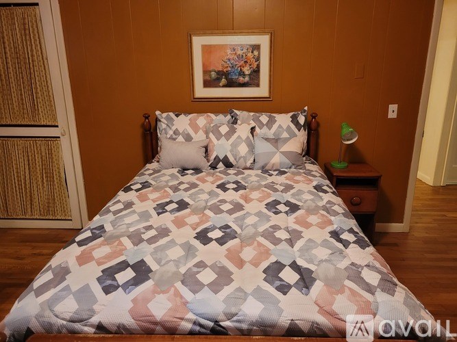 A bed with a patterned comforter and two pillows sits in a room with a wooden headboard.