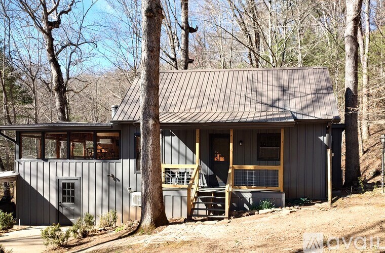 A small house with a grey roof and a brown door is surrounded by trees.