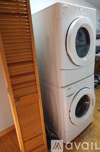 A white washing machine sits next to a wooden staircase.