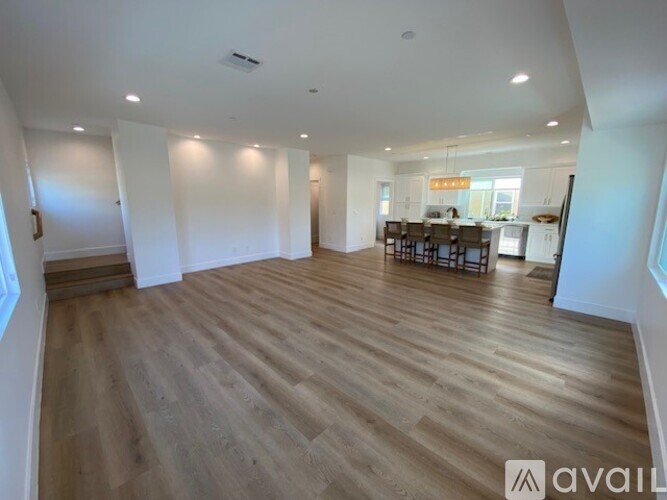 A spacious room with wooden flooring and a dining area in the background.