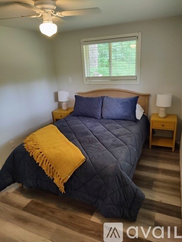 A bedroom with a bed covered in a blue comforter and a yellow throw.