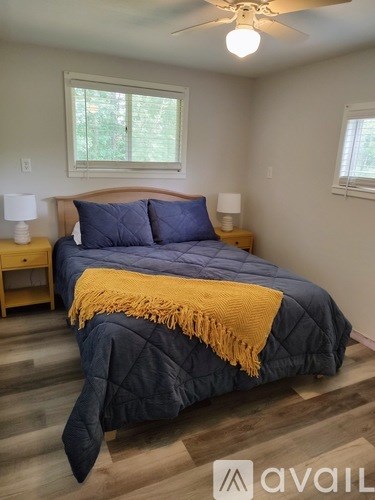 A bedroom with a bed covered in a blue comforter and a yellow throw.