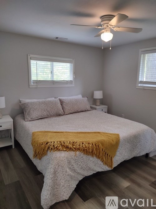 A bedroom with a bed covered in a white blanket and a yellow throw.