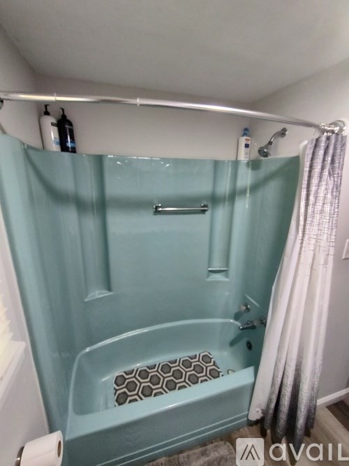 A blue bathtub with a shower curtain and a roll of toilet paper on the side.