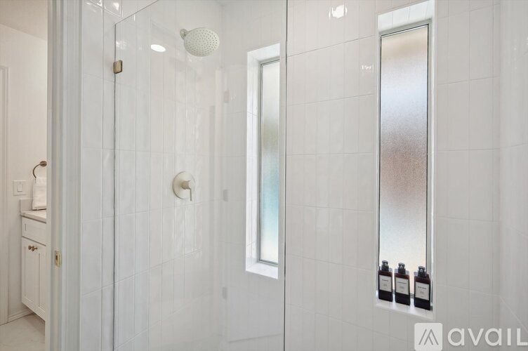 A white bathroom with a glass shower door and a white tiled wall.