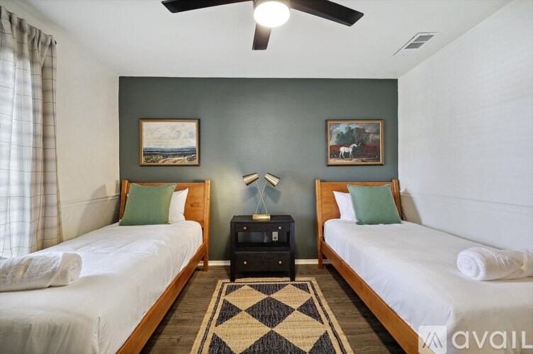 A room with two beds, a ceiling fan, and two pictures on the wall.